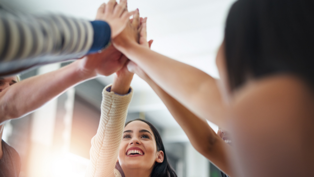 A group hold their arms up in unison, the woman in frame is smiling.