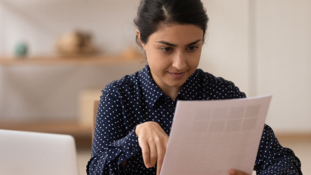 A woman in a polka dot shirt reads a piece of paper.